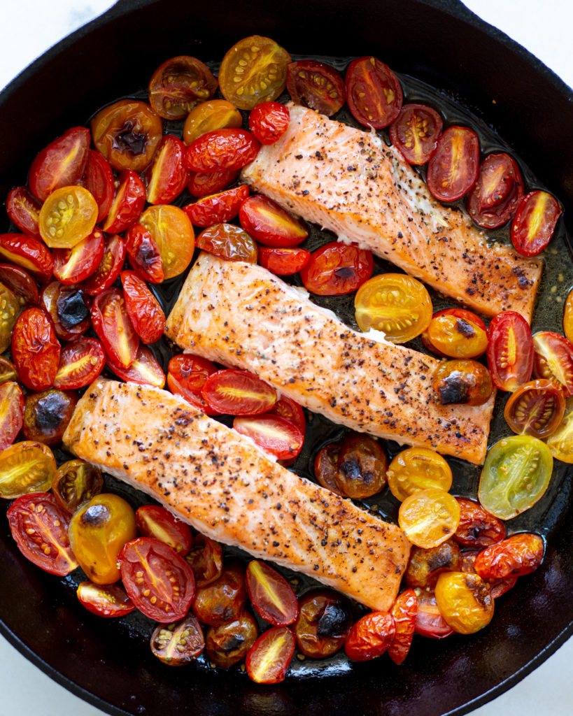 Cooked salmon and blistered tomatoes in pan