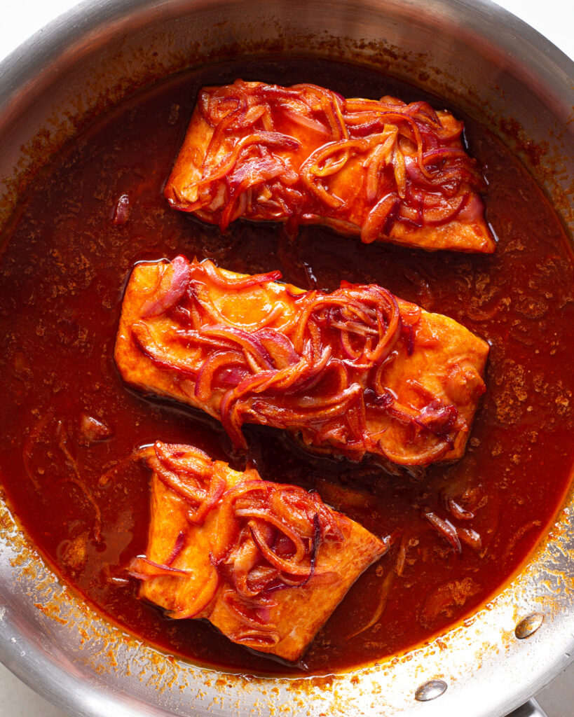 Salmon, sauce and onions in pan
