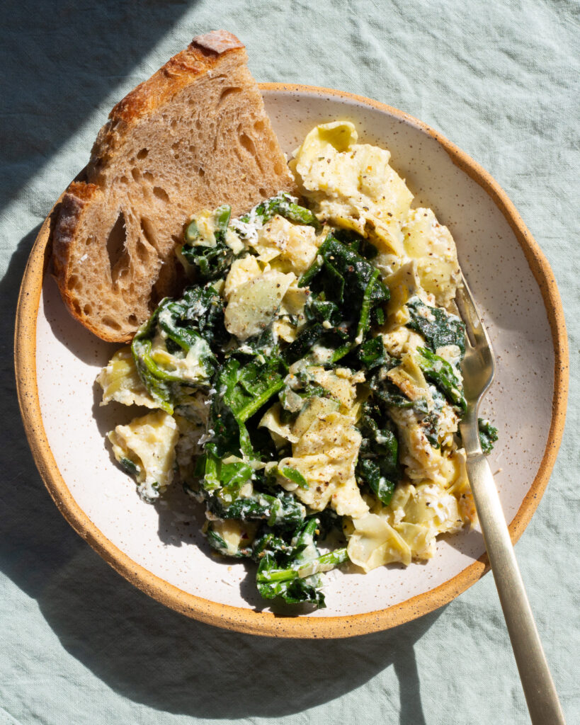 Spinach Artichoke Bowl plated for one, served with a slice of bread and a fork