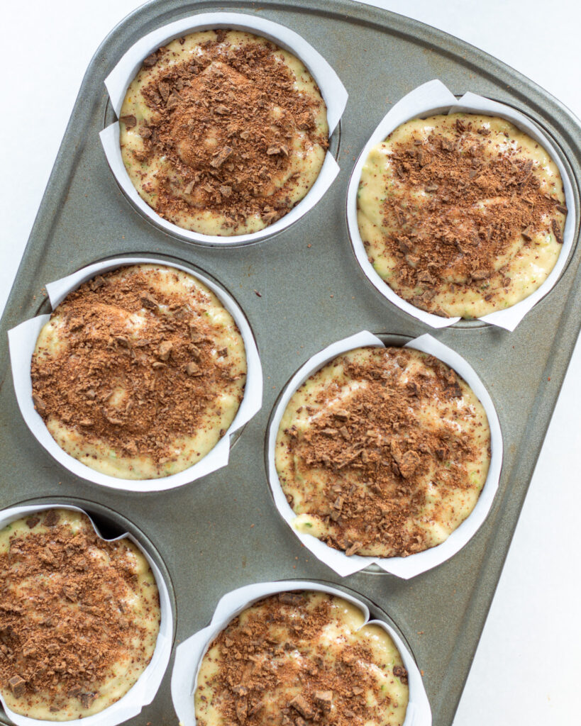 Zucchini muffin batter in muffin tin topped with cinnamon chocolate