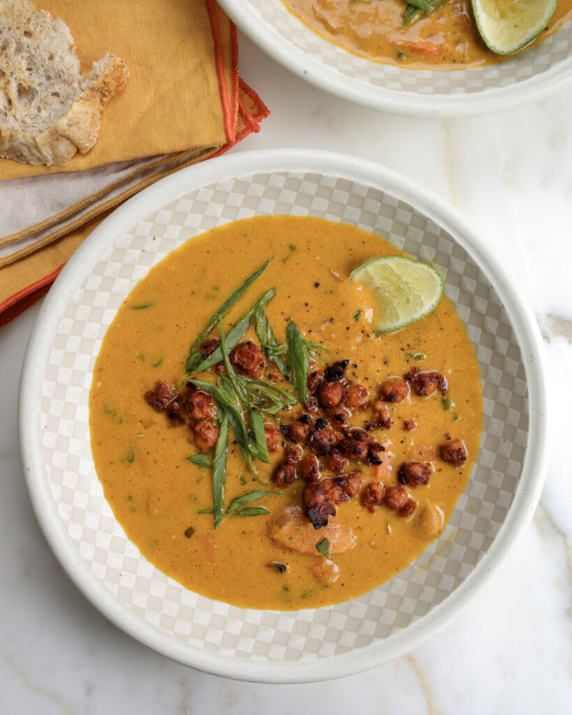 Carrot soup in a bowl topped with chickpeas and scallions.
