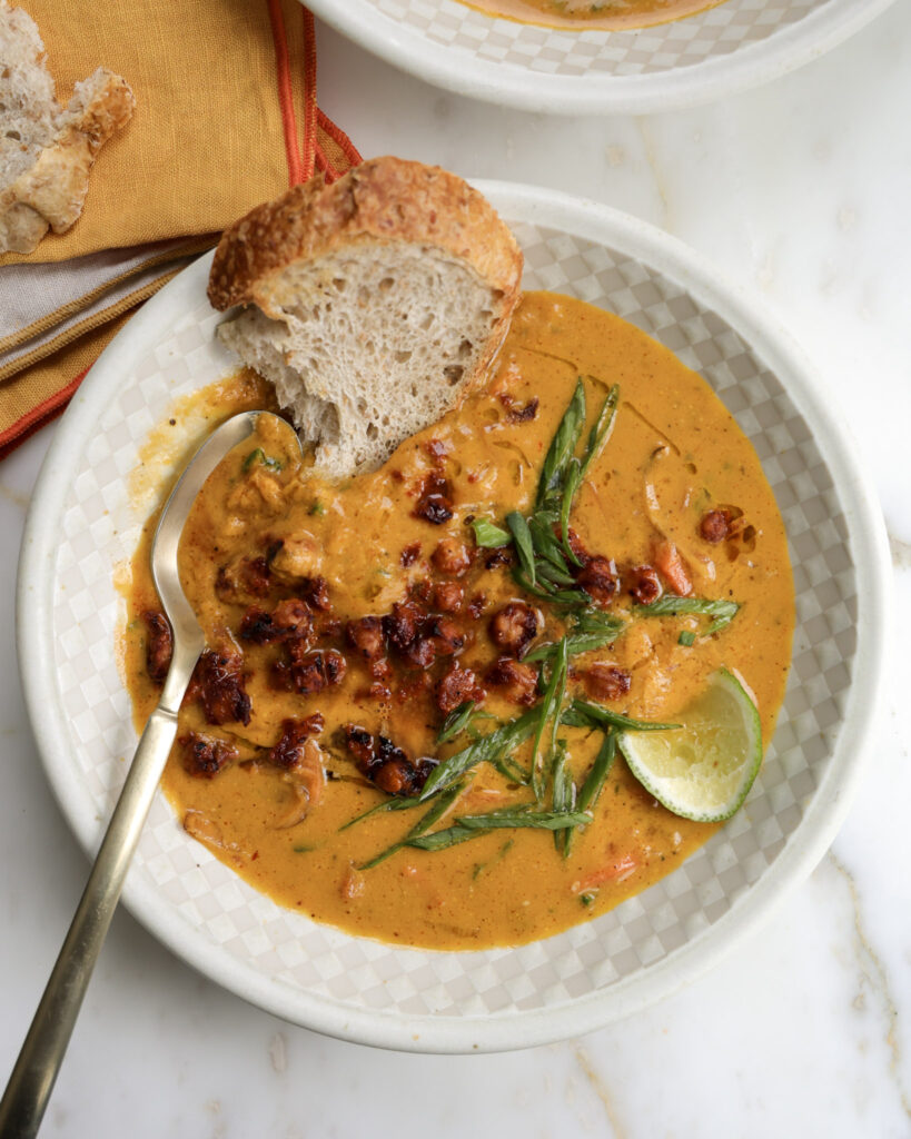 Carrot soup in a bowl topped with bread, chickpeas and scallions.