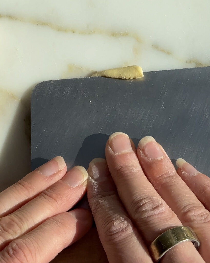 shaping homemade gemelli with a bench scraper.