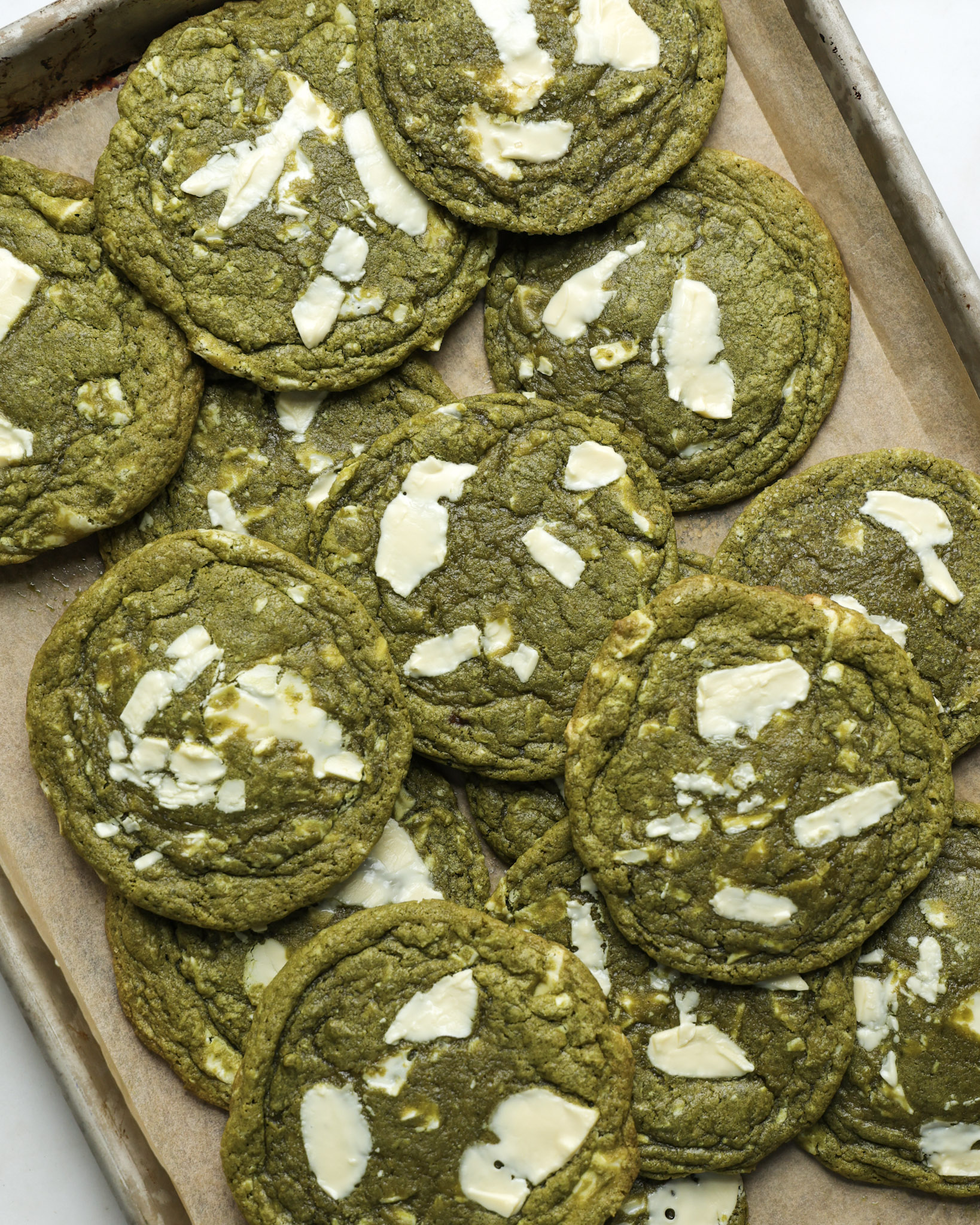 matcha cookies with chocolate chips piled on a baking sheet.