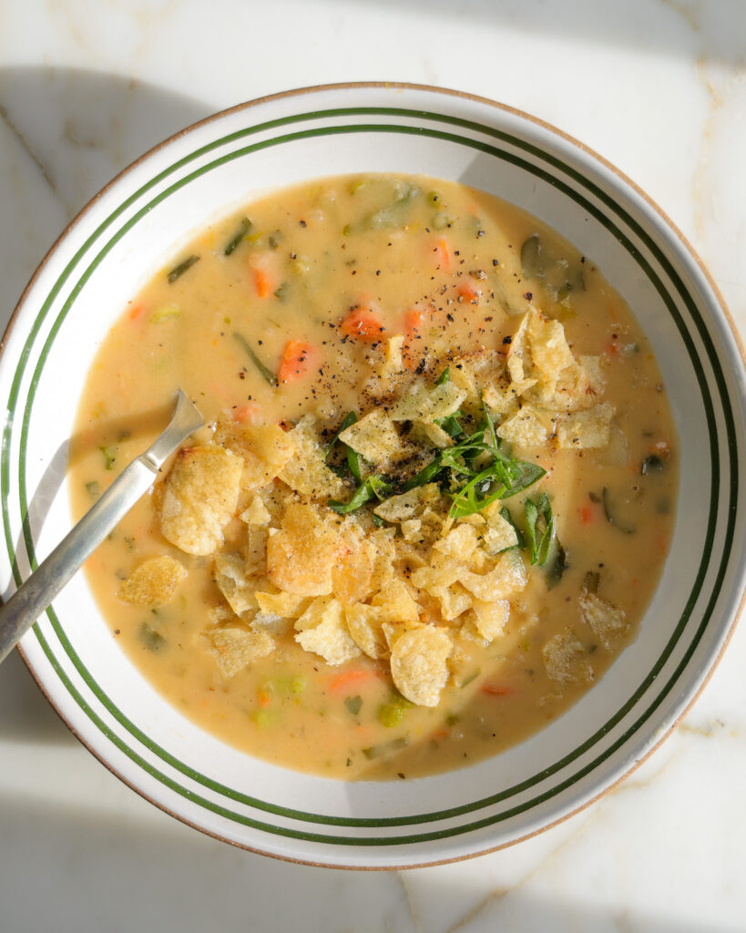 Close up of potato soup topped with scallions and salt and vinegar potato chips. 
