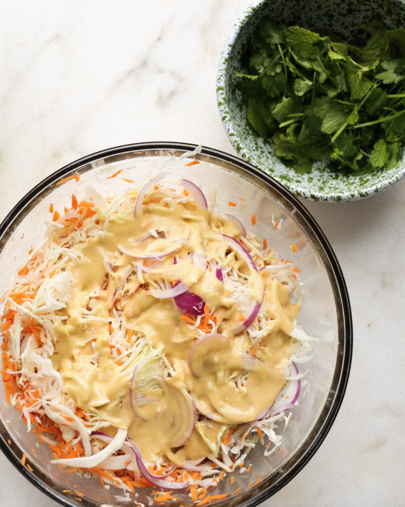 cabbage and carrot slaw in a bowl topped with ginger dressing.