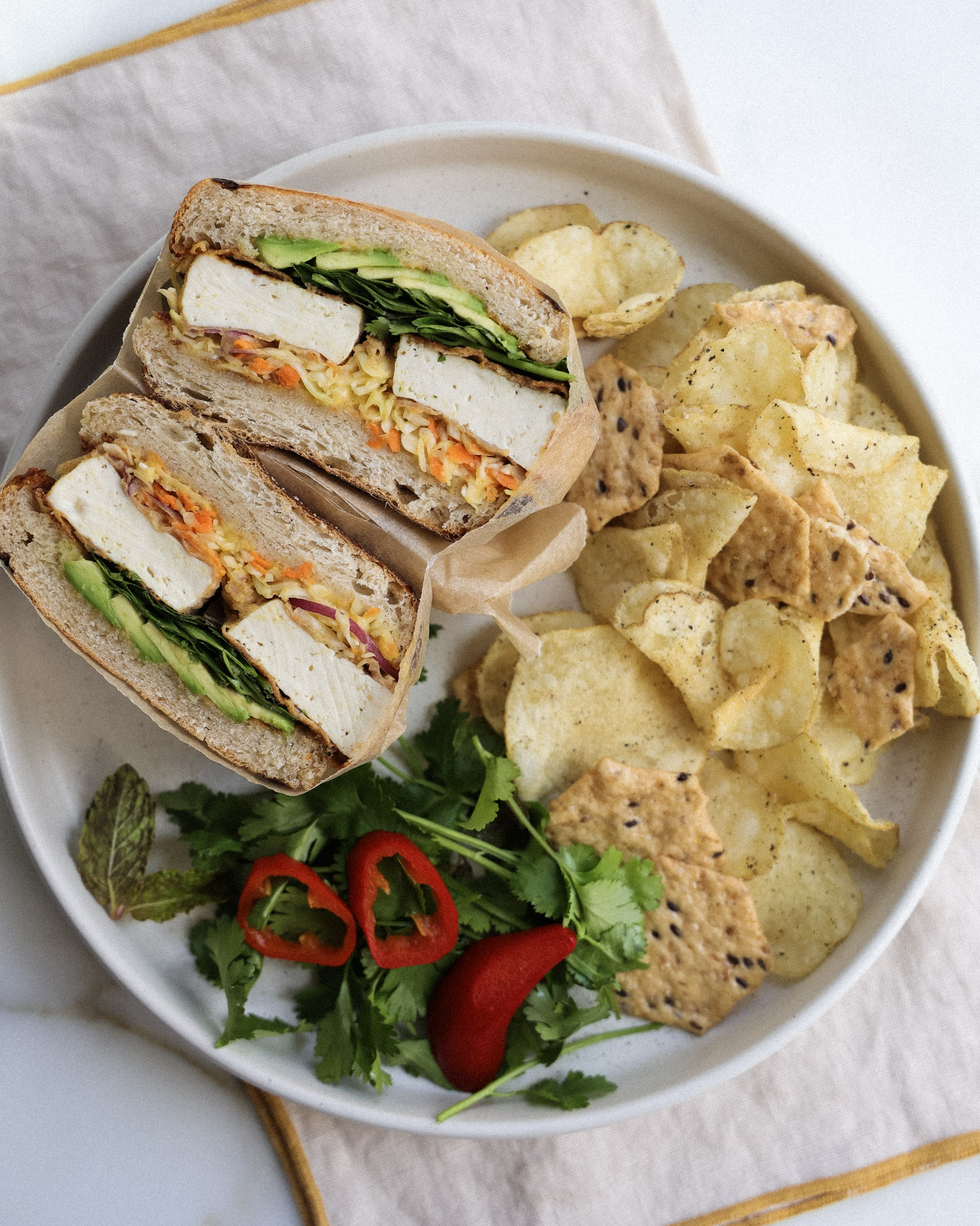 tofu sandwich served with chips and veggies.