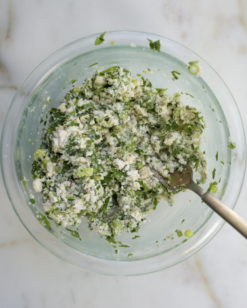 goat cheese and herbs being mixed in a bowl.