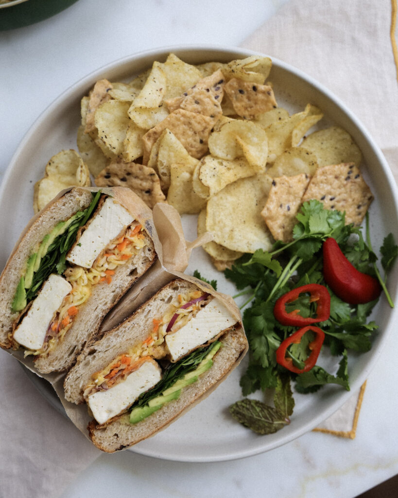 baked tofu sandwich served with chips and veggies.