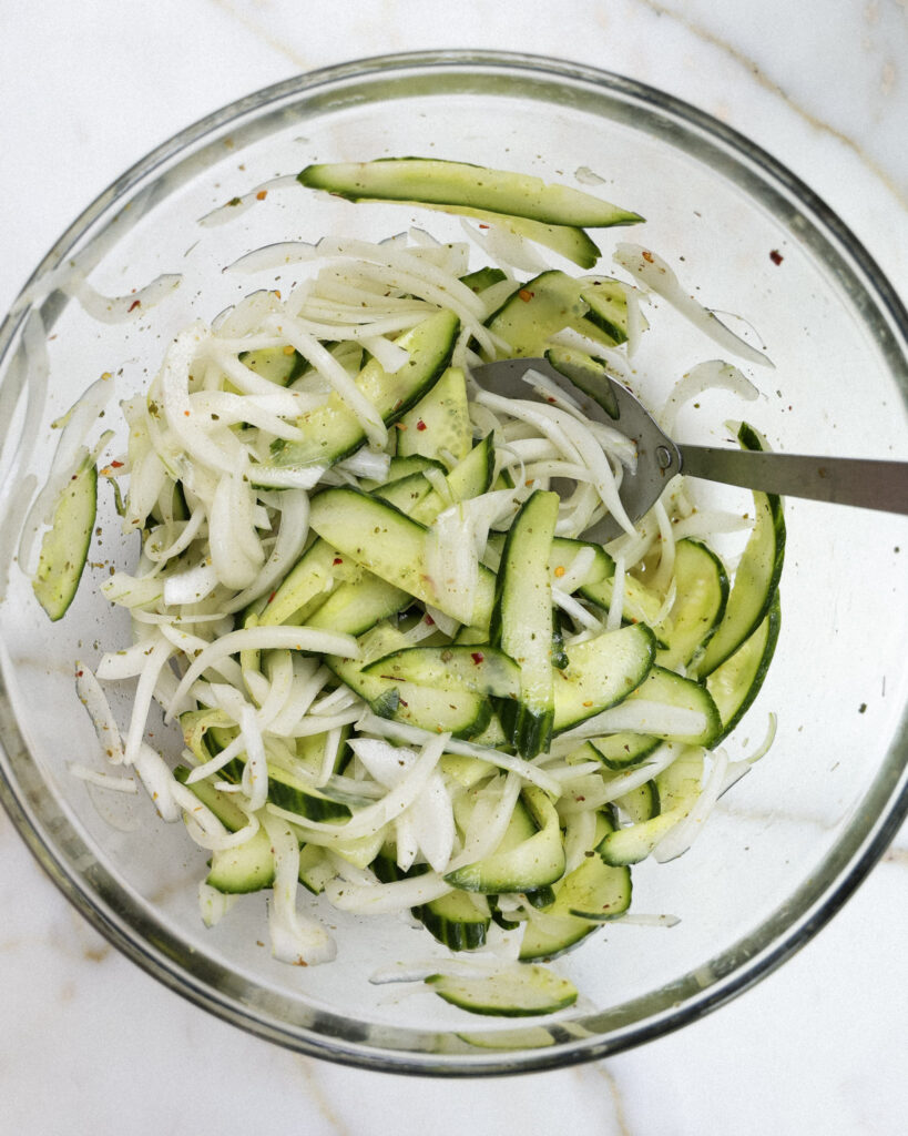Cucumber and onion tossed with spices in a bowl.