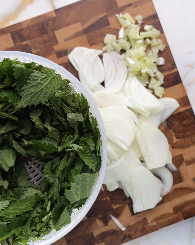 stinging nettles, onion and garlic on a cutting board.