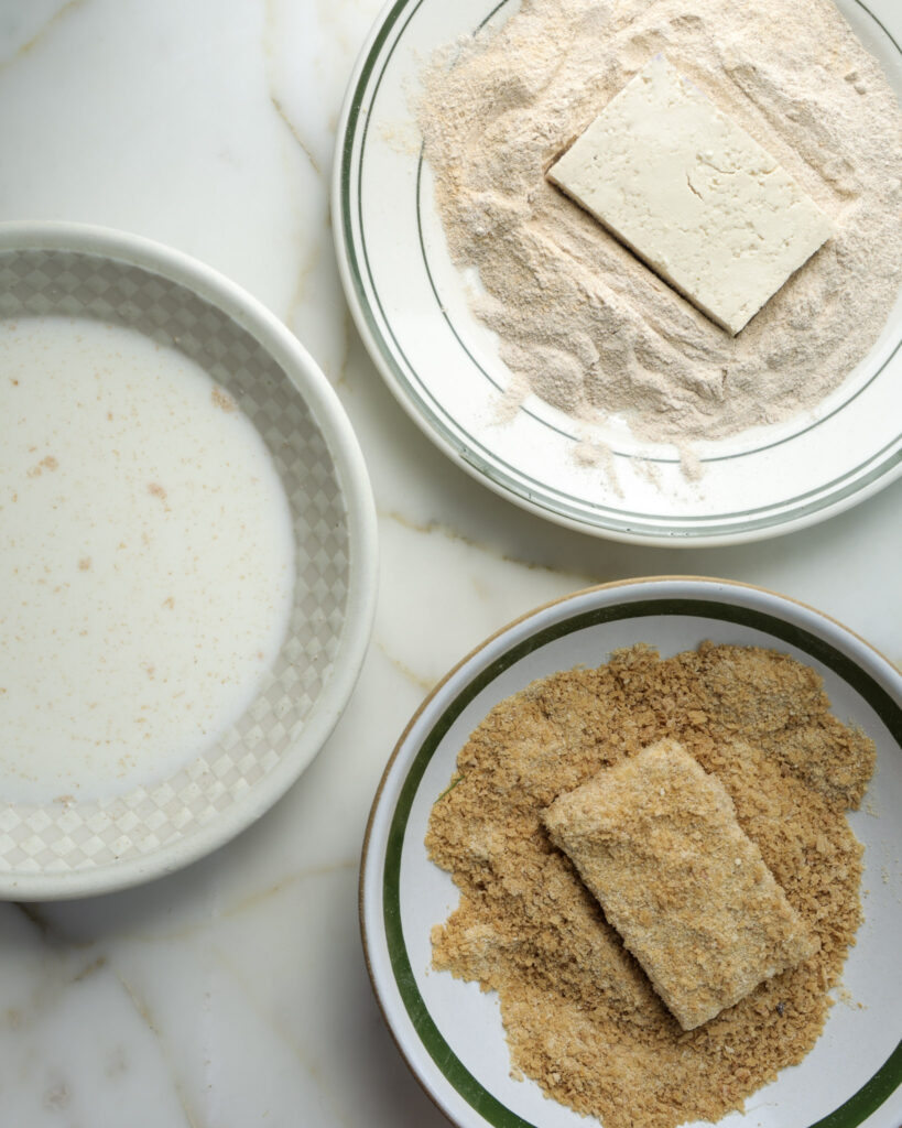 Tofu cutlets being dredged and breaded.