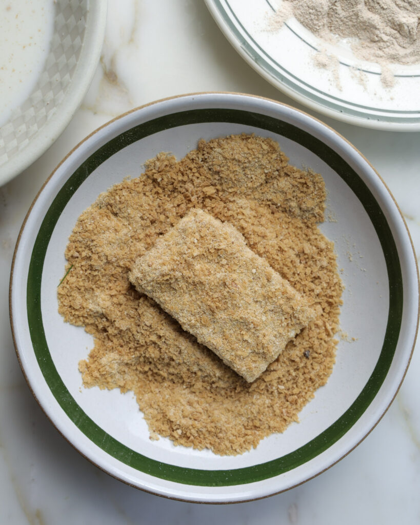 Tofu slices being coated in bread crumbs.