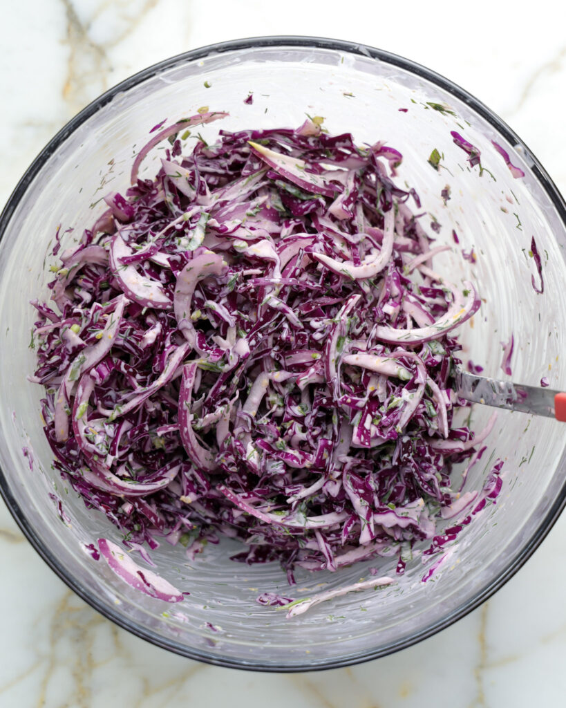 Cabbage slaw being mixed in a bowl.