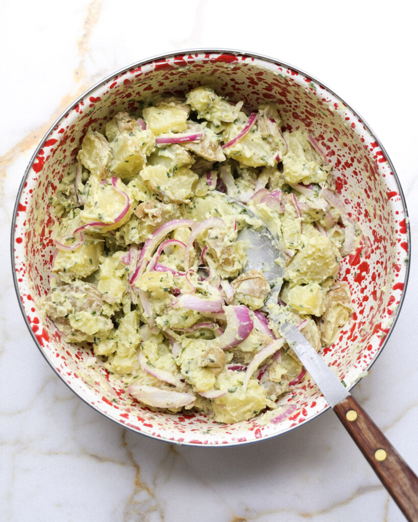 Basil potato salad being mixed in a bowl.