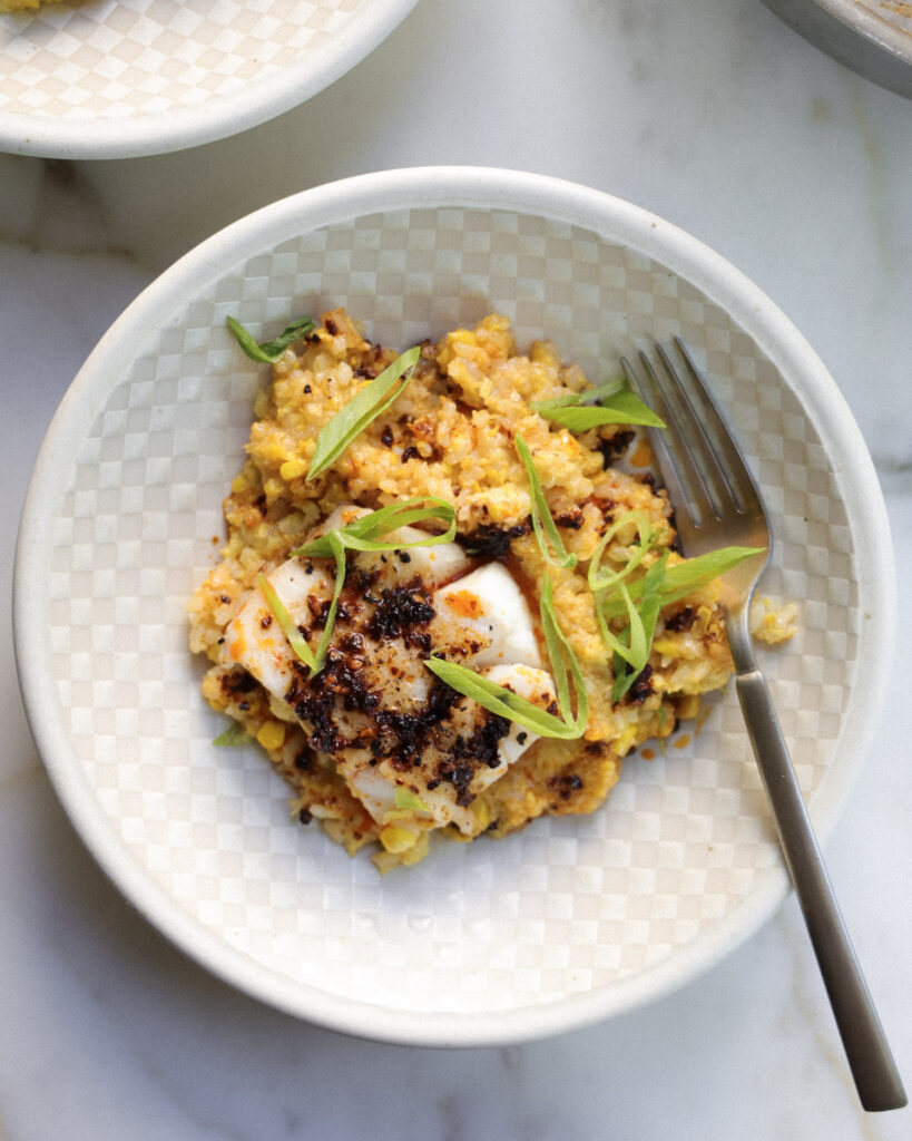 Cod over miso corn rice topped with scallions and chili crisp on a plate.