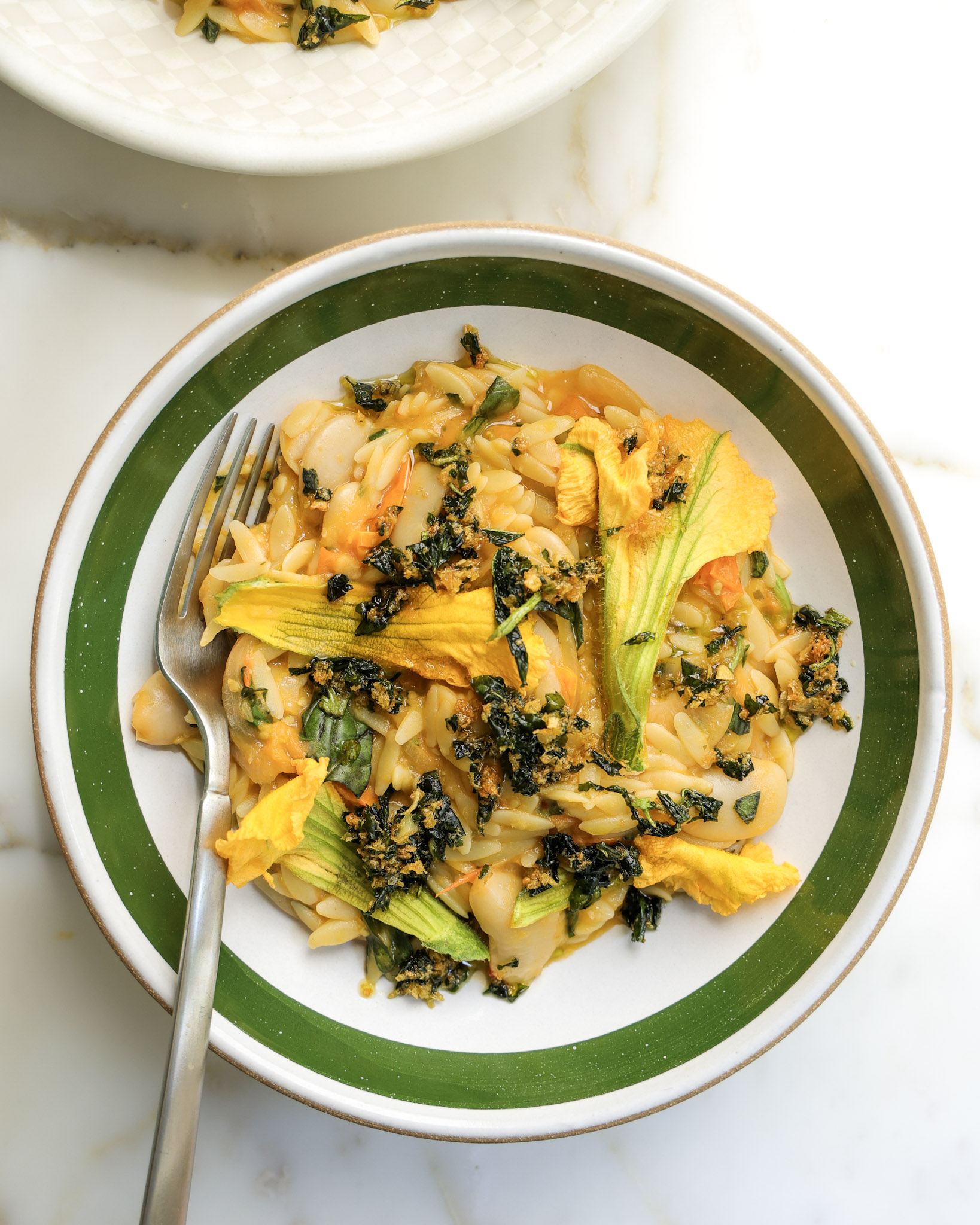 Sungold tomato orzo in a bowl topped with squash blossoms