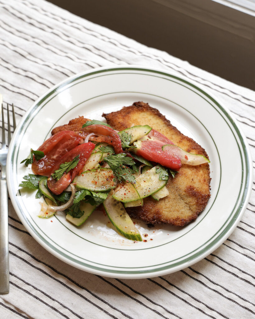Tomato salad spooned over fried tilapia on plate.