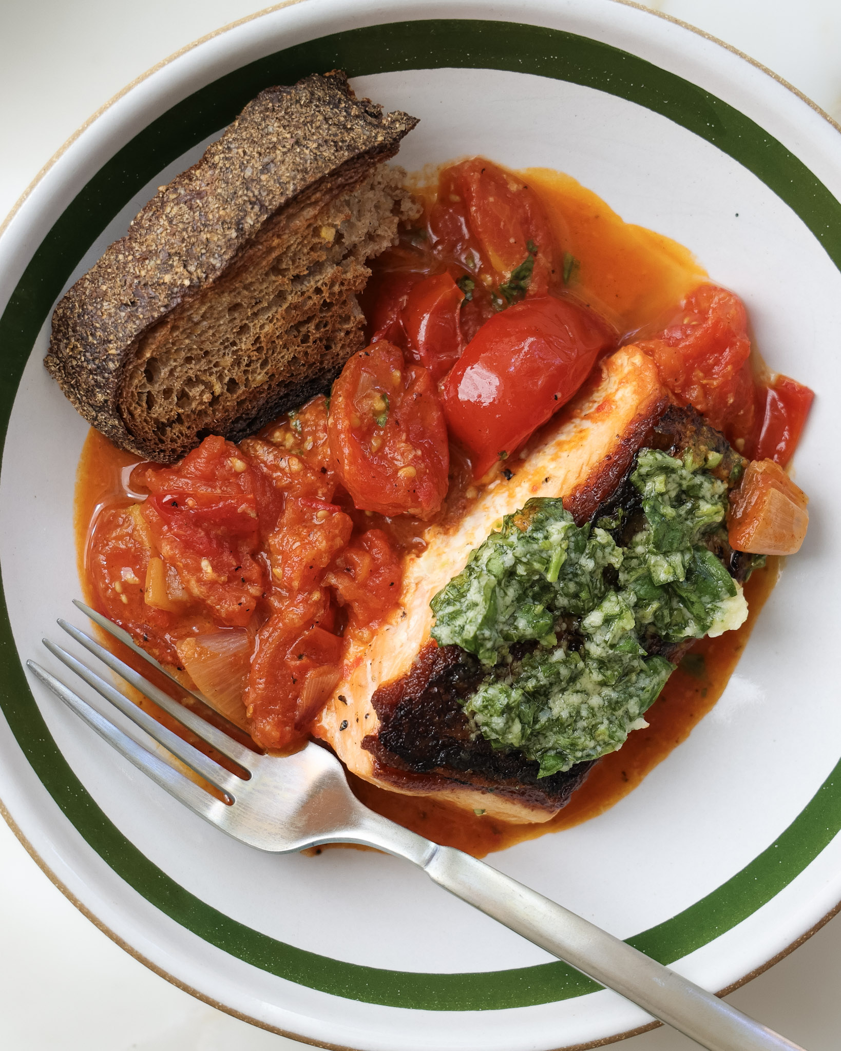 Basil tomato salmon in a bowl with a slice of sourdough.