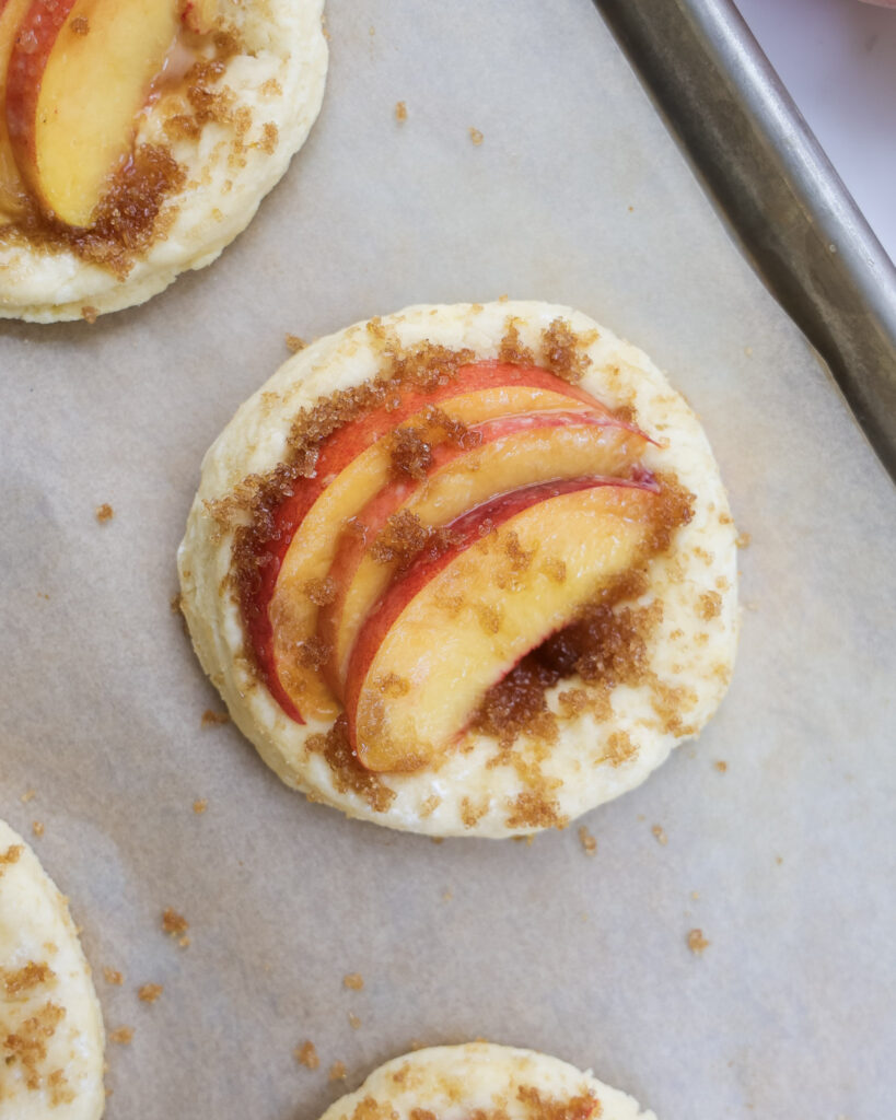 Unbaked shortcakes topped with peaches.