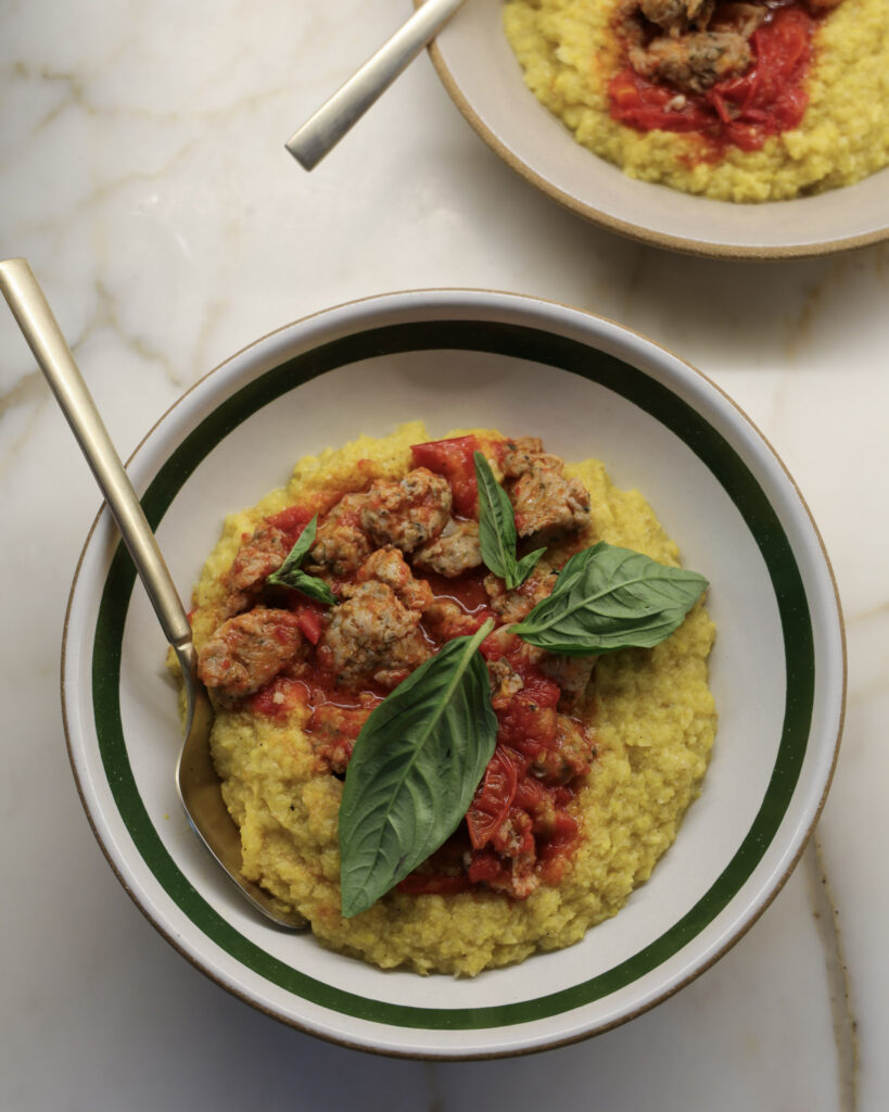 Fresh polenta & tomato sausage topped with basil in a bowl.