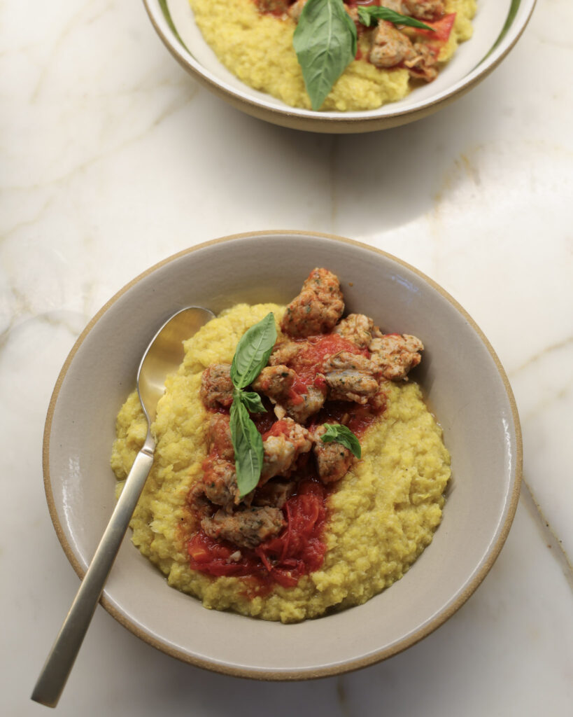 Fresh polenta & sausage topped with sauce and basil in a bowl.
